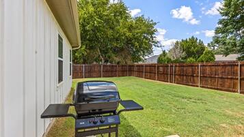 A backyard with a barbecue grill, a wooden fence, and a house.