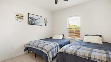 A bedroom with two beds, a ceiling fan, a window with blinds, and wall decorations including a framed picture and a dreamcatcher.