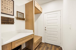 A hallway with a white door, wooden cabinets, a white countertop, and a wall-mounted animal track chart. - Twin Lake Homes - Sleeps 16 Fire Pit Swing (Granbury)