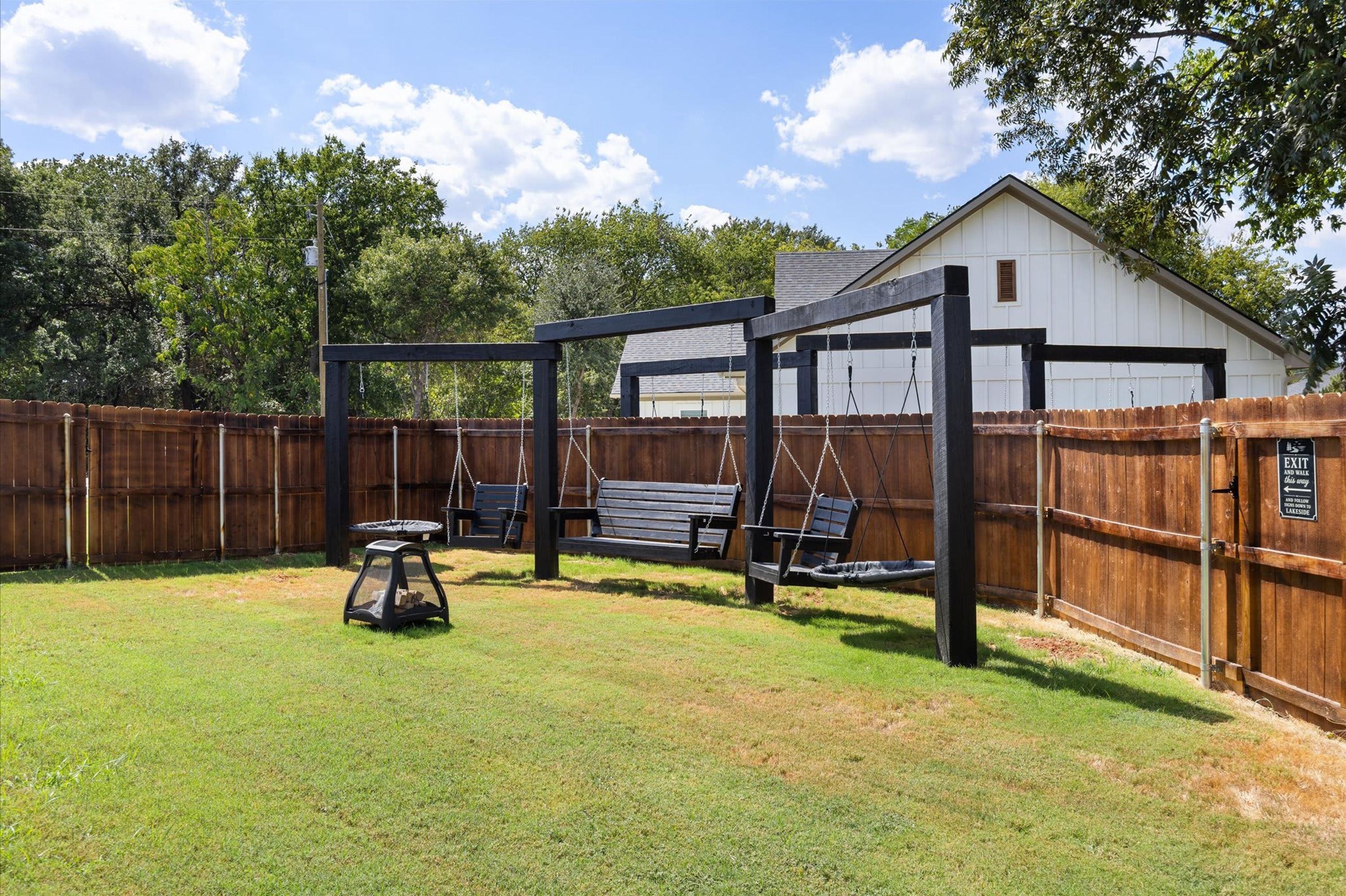 A backyard with a wooden swing set, a small table, and a covered seating area.