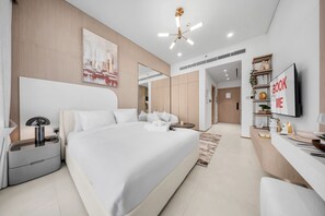 Ein modernes Hotelzimmer mit einem großen Bett, einem Schreibtisch, einem Sessel, einem Fernseher und einem Bücherregal.