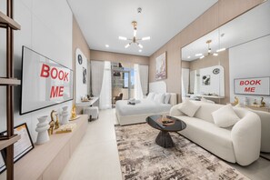 Ein modernes Hotelzimmer mit einem großen Bett, einer Couch, einem Schreibtisch und einem Fernseher, der 'BOOK ME' anzeigt.