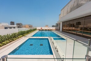 Ein Pool auf dem Dach mit klarem, blauem Wasser, umgeben von Glasgeländern und einer Reihe von Liegestühlen.