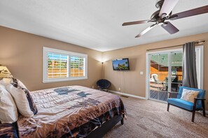 Un dormitorio con una cama, ventilador de techo, televisor y vistas al exterior a través de un ventanal corredero.