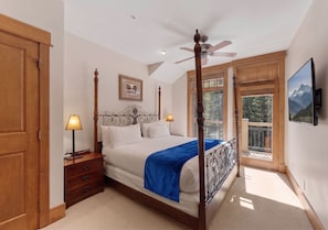 A four-poster bed with a blue throw, a nightstand with a lamp, and a large window with a mountain view. - Slope View | King Beds | Ski in/Ski Out (Keystone)
