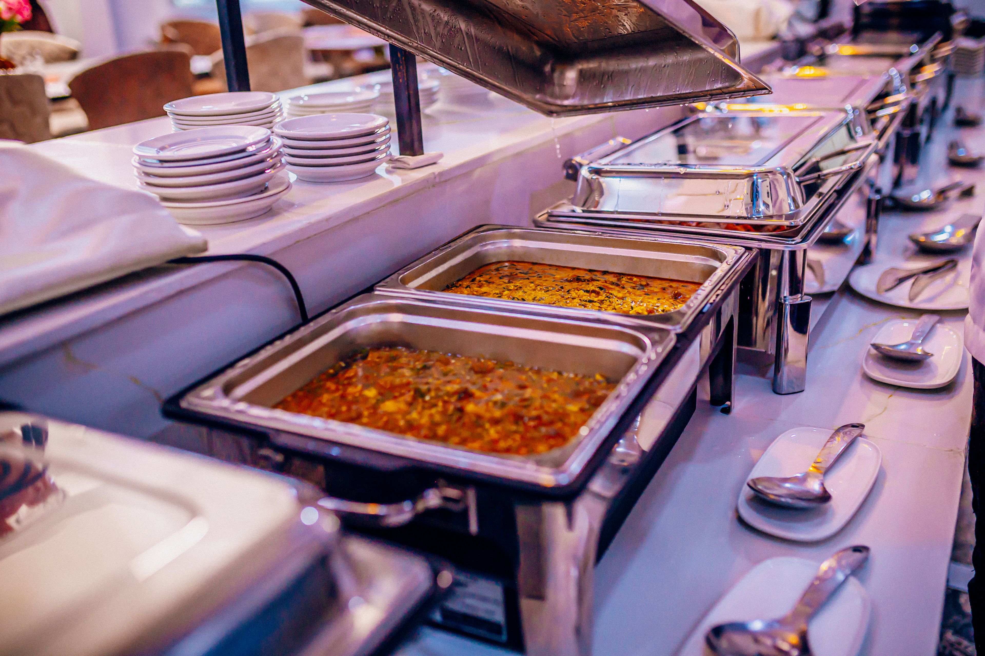 A buffet setup with multiple serving trays and stacked plates.