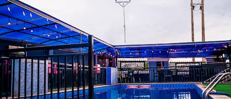 A swimming pool with a blue roof, surrounded by a fence and a grassy area.