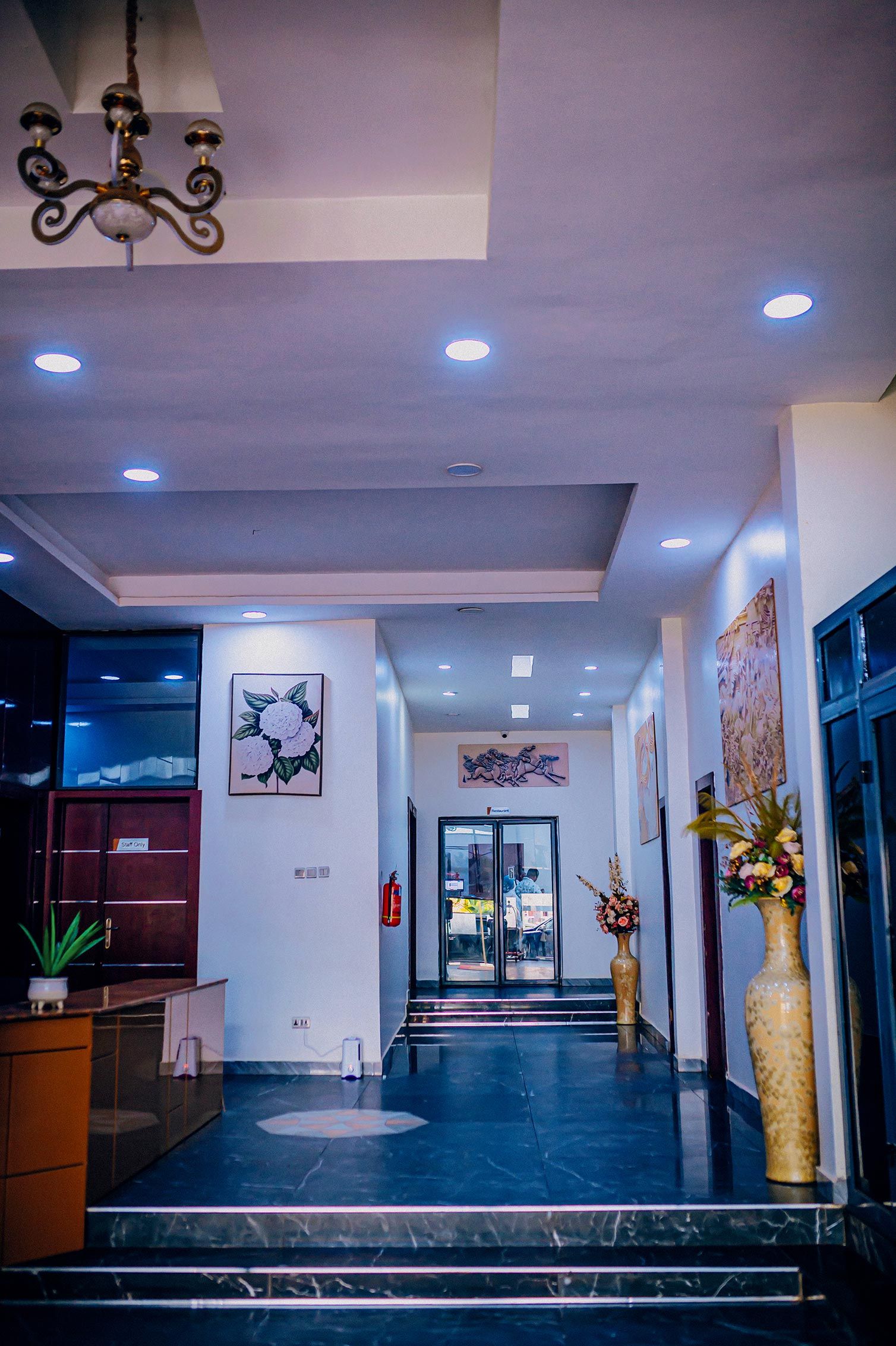 Un hall de hotel con mostrador de recepción, una escalera que sube a los pisos superiores y una entrada con puerta de vidrio.