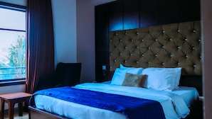 Ein Hotelzimmer mit einem großen Bett, einem Nachttisch, einem Sessel und einem Fenster mit Vorhängen.