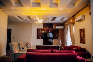 Habitación de hotel con sofá, televisor y una lámpara decorativa con forma de mano en el techo.