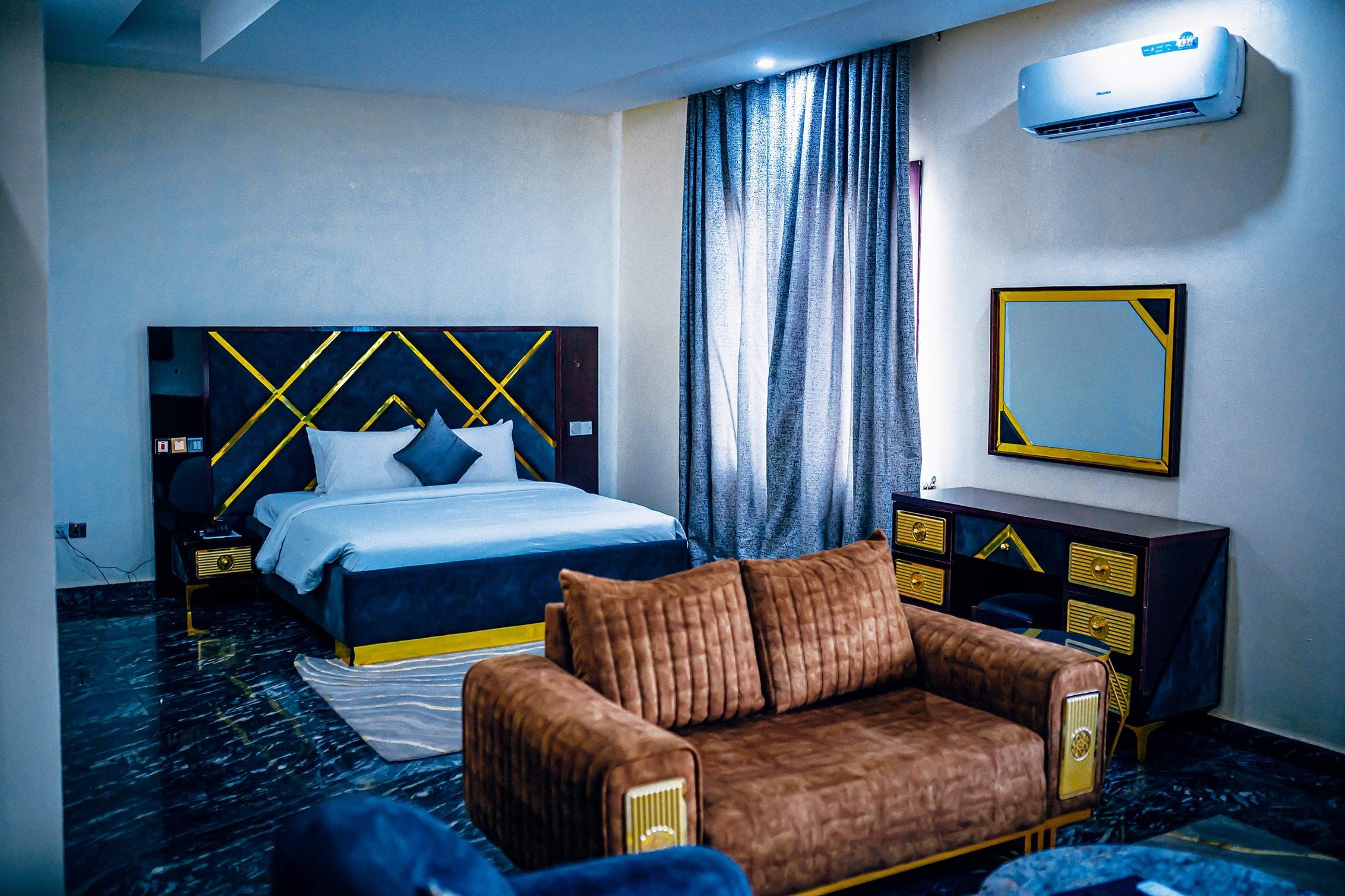 Quarto de hotel com cama, sofá, cômoda e ar condicionado.