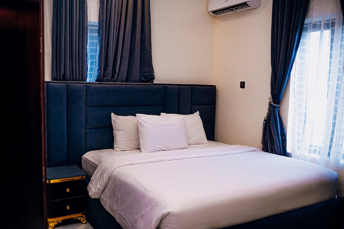 A hotel room with a large bed, a nightstand, and a wardrobe.