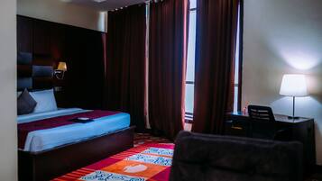 A hotel room with a bed, a desk, a chair, a lamp, and a window with curtains.