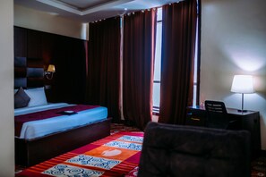 Habitación de hotel con cama, escritorio, silla, lámpara y ventana con cortinas.