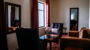 Una habitación con un sillón oscuro, un sofá, una mesita con un jarrón de flores y un espejo grande en la pared.