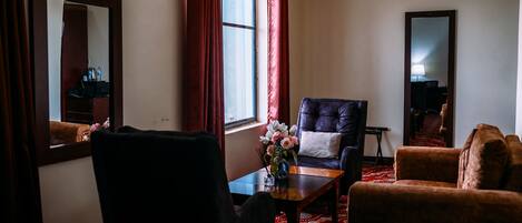 Una habitación con un sillón oscuro, un sofá, una mesita con un jarrón de flores y un espejo grande en la pared.