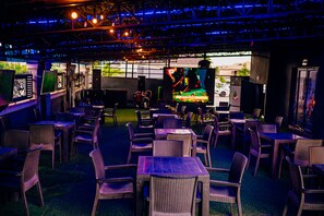Un comedor interior con mesas y sillas, un escenario con un artista, y vista a la calle.
