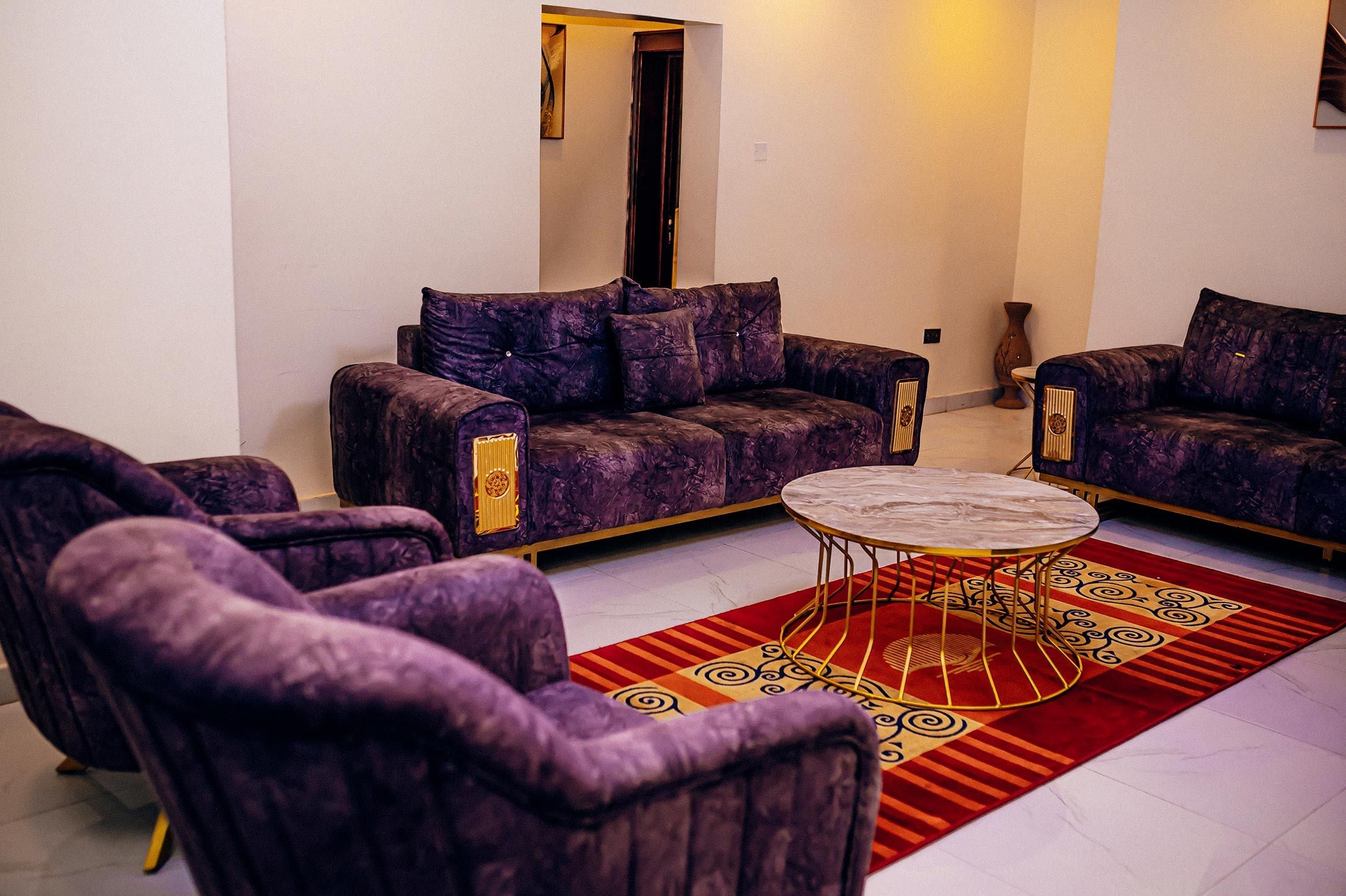 Uma sala de estar com sofá roxo, mesa de centro redonda e tapete estampado.