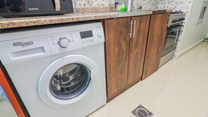 Eine kompakte Küche mit Waschmaschine, Holzschränken und einer Mikrowelle.