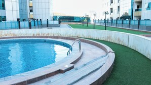 En swimmingpool med en klar, blå vandoverflade, omgivet af en stenterrasse og et område med grøn kunstgræs.