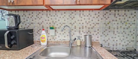 A kitchen with a stainless steel sink, a kettle, a bottle of Fairy dish soap, and a grater.
