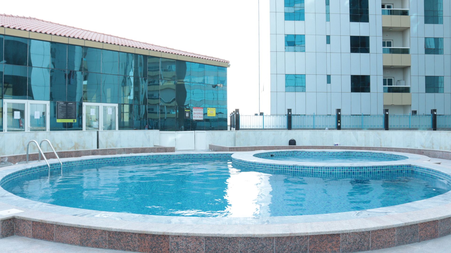 Una piscina con bordo piastrellato, circondata da un muretto basso e un edificio sullo sfondo con finestre a specchio.