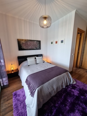 A bedroom with a bed, a hanging light fixture, a painting, and a door.
