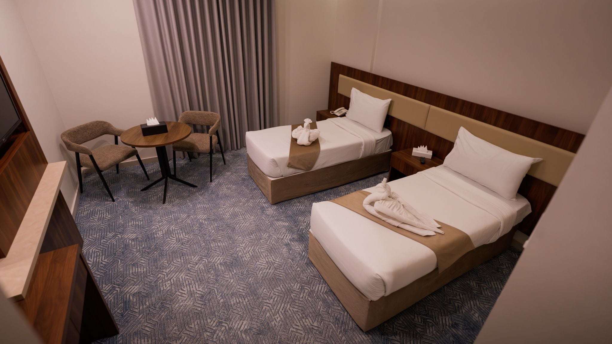 Habitación de hotel con dos camas, un escritorio, una silla y un televisor.