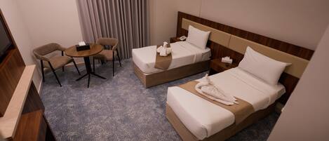 Habitación de hotel con dos camas, un escritorio, una silla y un televisor.