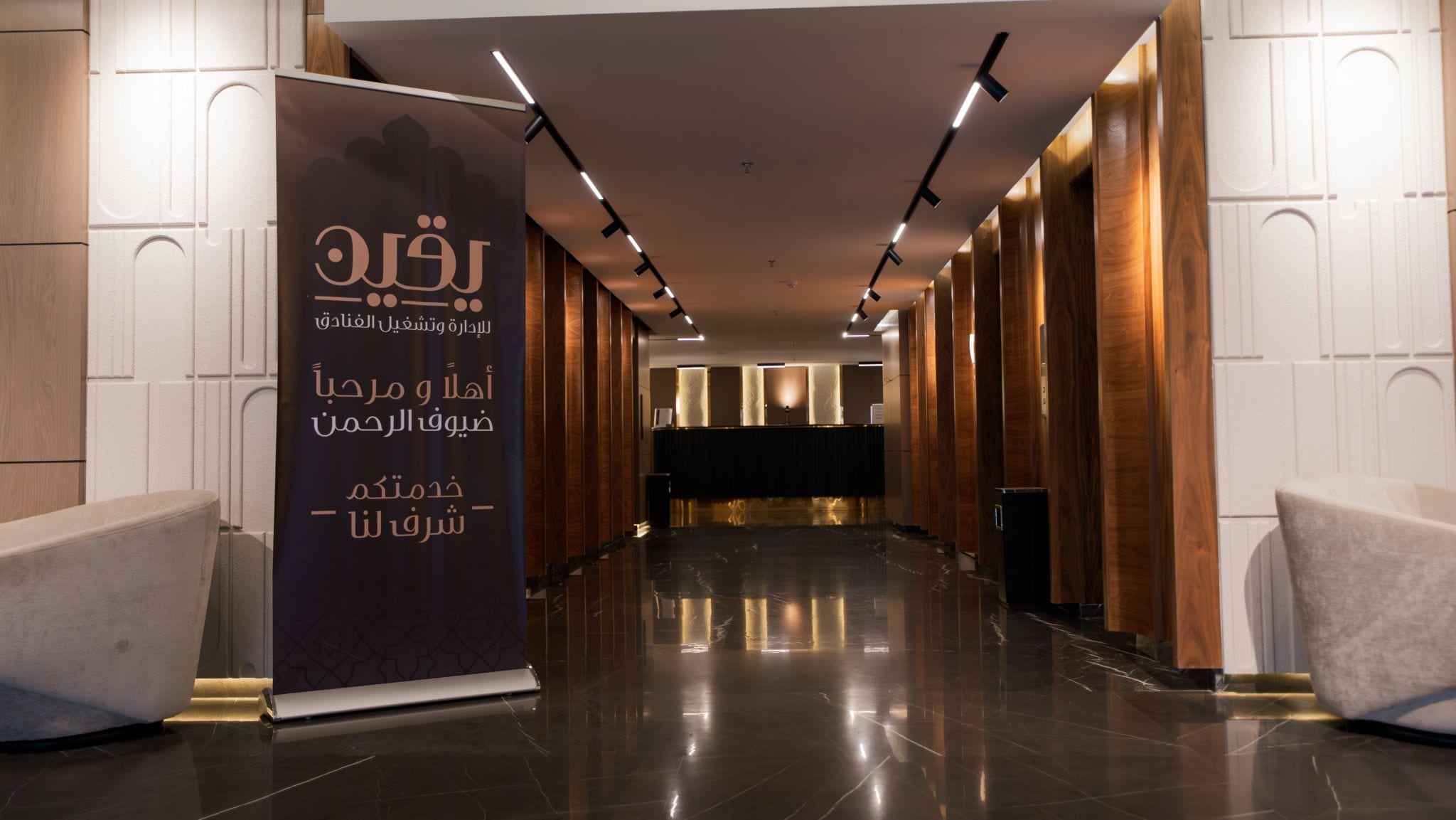 A hotel lobby with a reception desk, a large informational stand, and a polished marble floor.