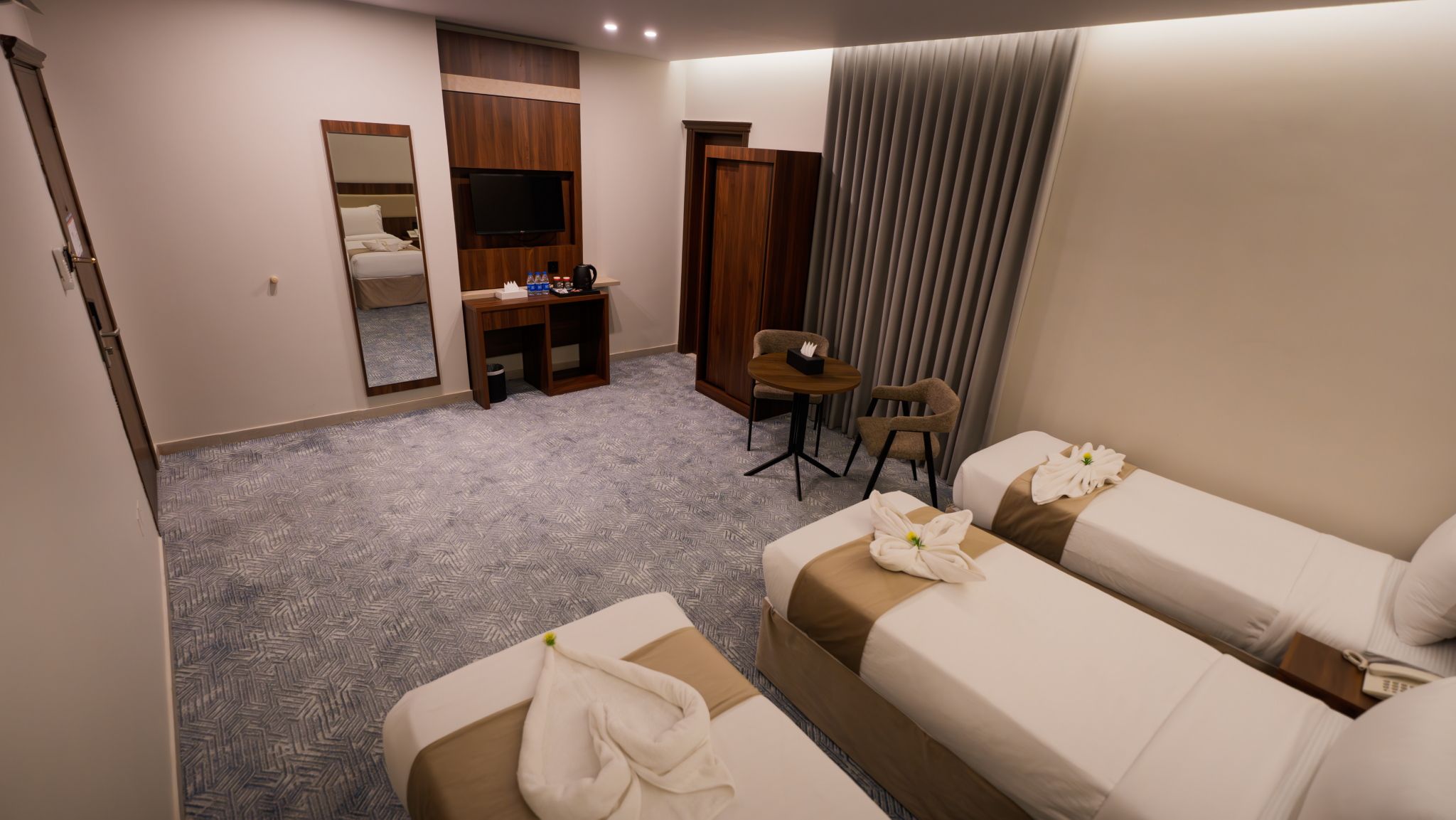 A hotel room with two beds, a desk, a chair, a TV, and a wardrobe.