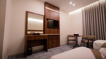 Habitación de hotel con cama, escritorio con televisor, una pequeña mesa con sillas y ventana con cortinas.