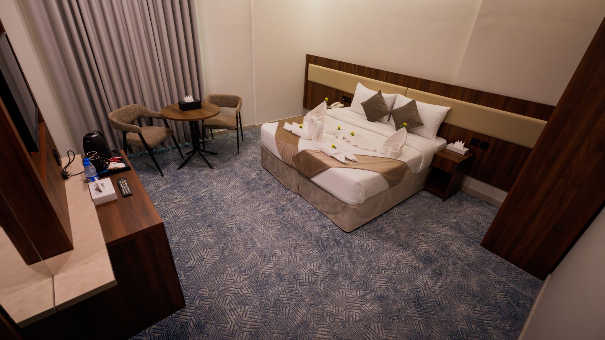 A hotel room with a bed, bedside tables, a desk, and a chair.