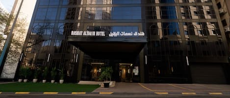 En moderne hotelindgang med en glasfacade, arabisk skilte og et velholdt område.
