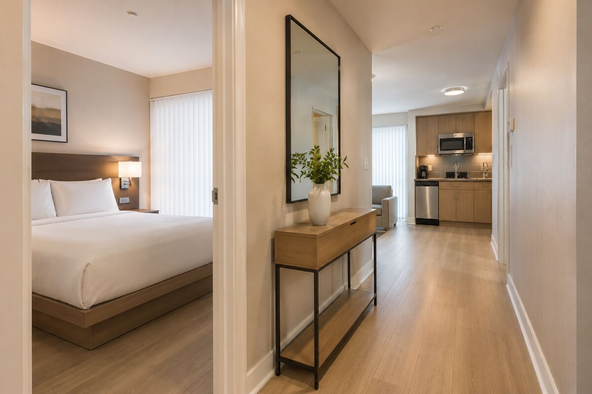 Ein Hotelzimmer mit Bett, Nachttisch und einem großen Spiegel. Es gibt eine kleine Küchenzeile mit einer Mikrowelle und einem Spülbecken.