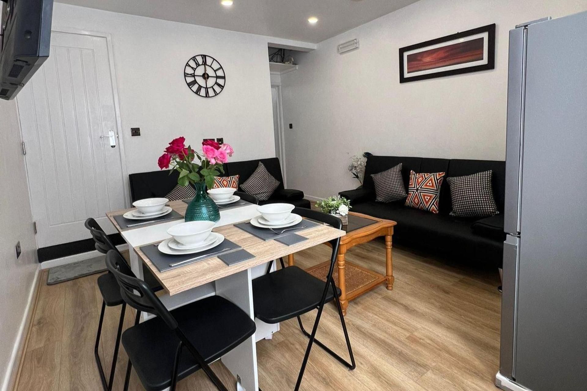 A modern dining area with a wooden table, black chairs, and a black sofa with patterned cushions.
