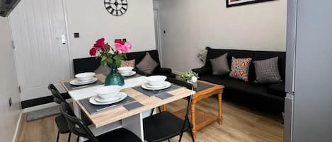 A modern dining area with a wooden table, black chairs, and a black sofa with patterned cushions.