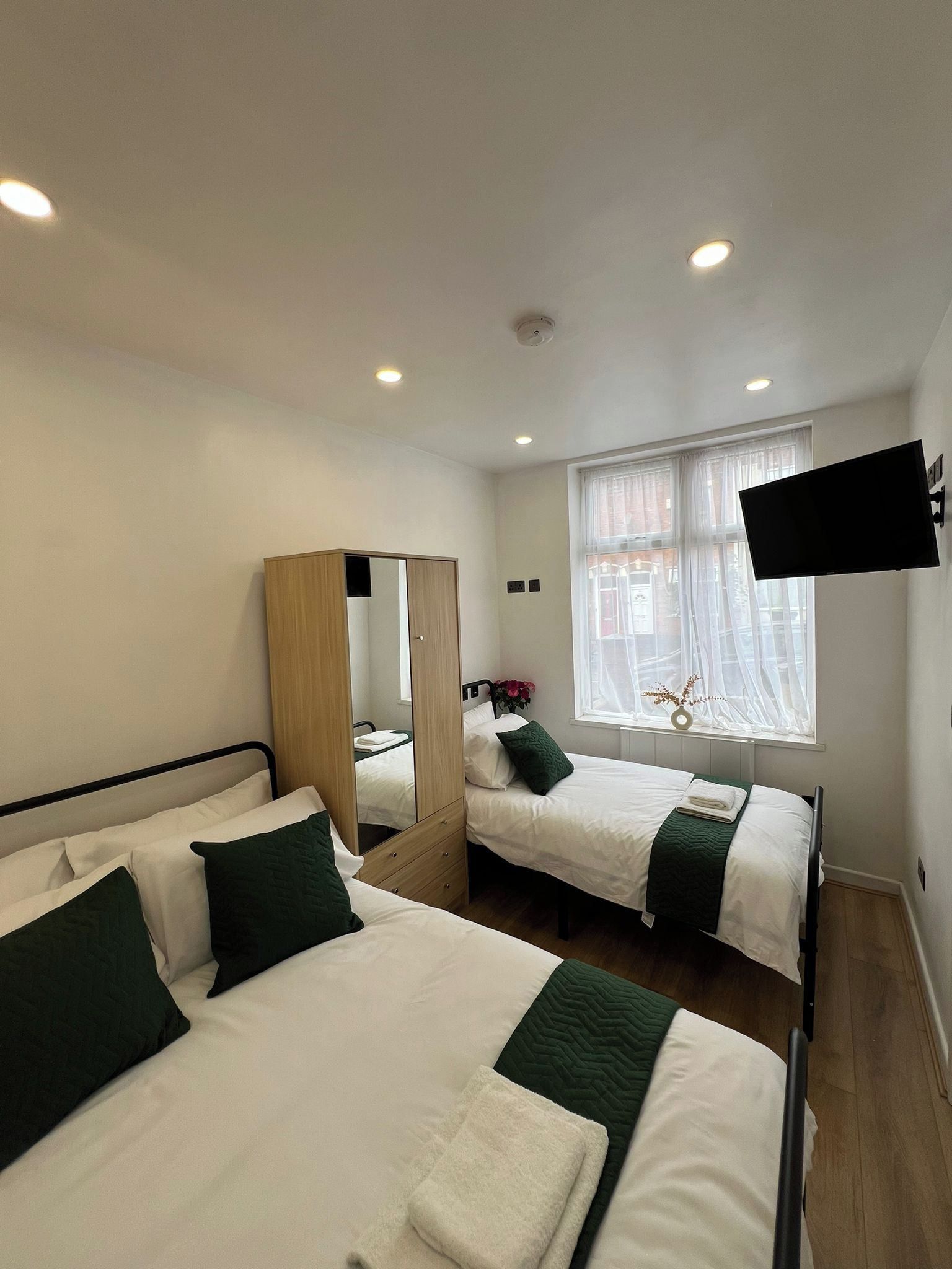 A hotel room with two beds, a wardrobe, a mirror, a flat-screen TV, and a window with a view.