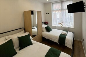 A hotel room with two single beds, a wardrobe, a flat-screen TV, and a window with sheer curtains. - Florence House Sleeps 13 - Free Parking & Garden (West Bromwich)