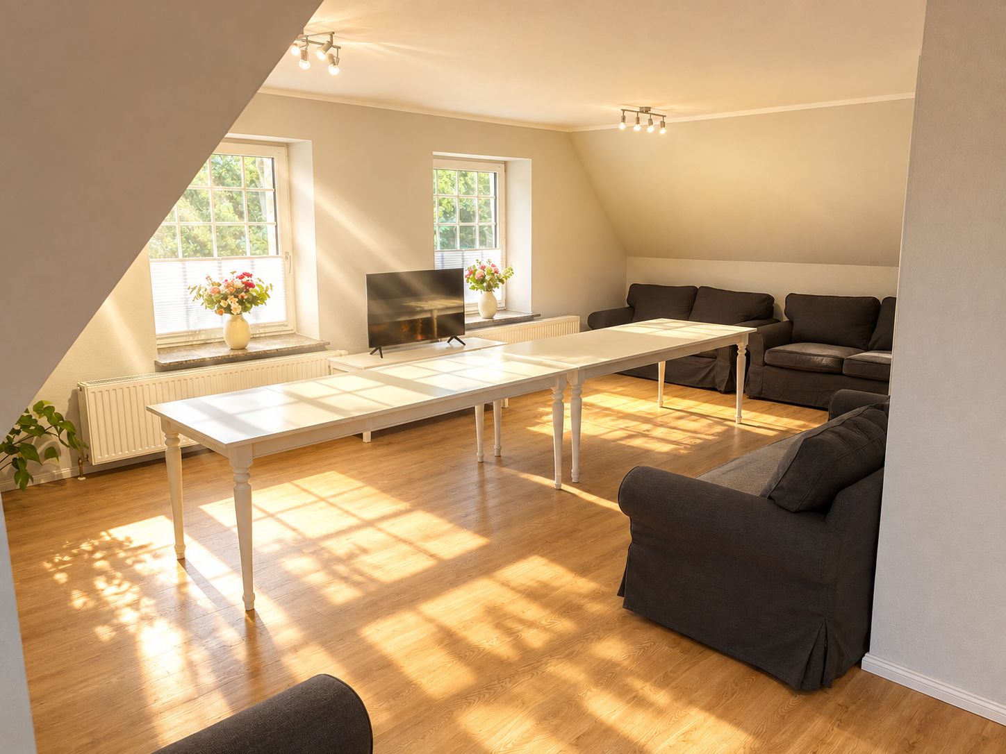 Ein modernes Wohnzimmer mit einem weißen Tisch, dunklen Sofas und einem Flachbildfernseher.