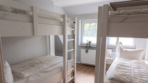 A bunk bed room with a window, a radiator, and a desk with a plant.