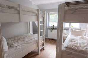 Une chambre avec un lit superposé, une fenêtre, un radiateur et un bureau agrémenté d’une plante.
