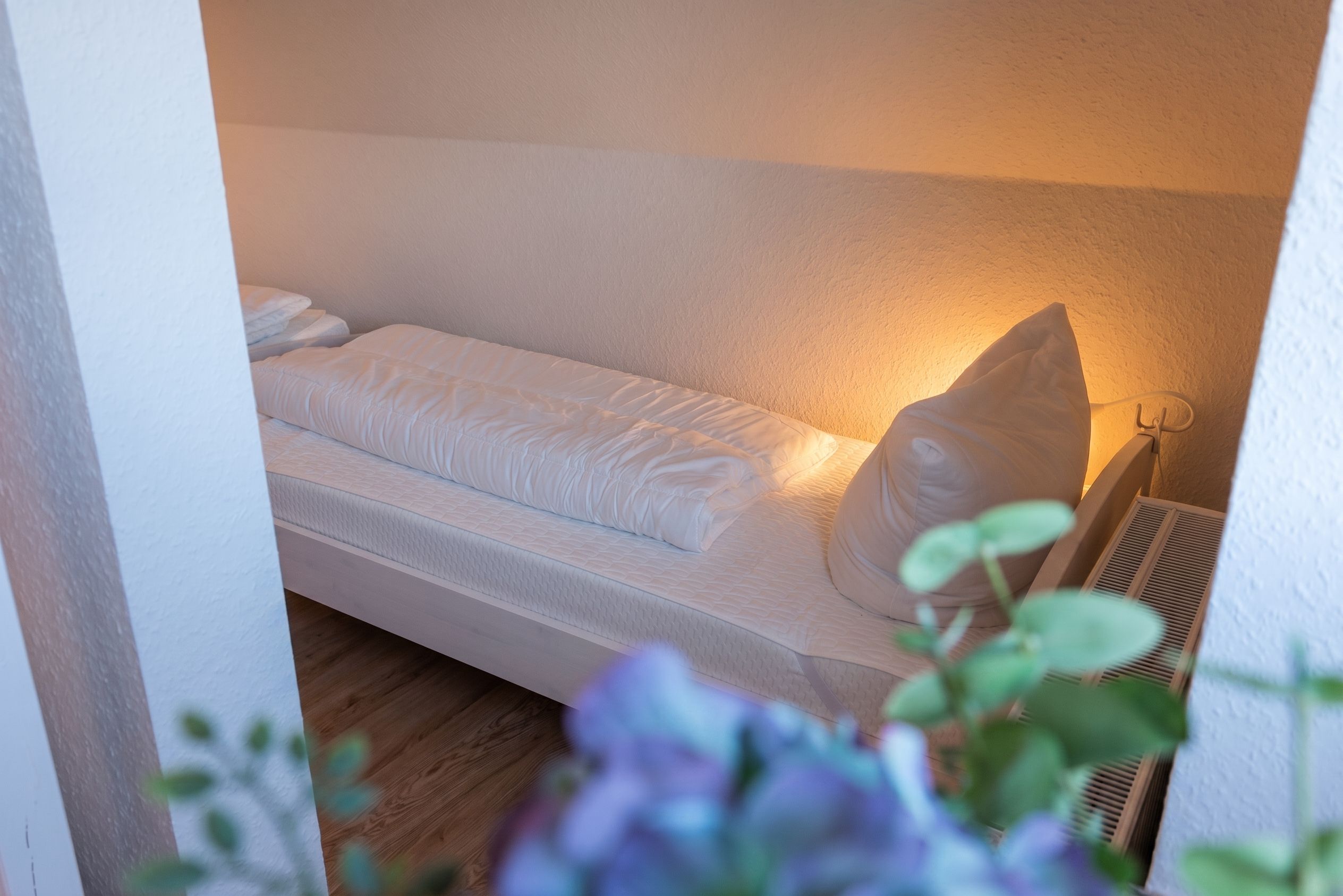 Un lit simple avec un oreiller et une tête de lit, une table de chevet et un radiateur fixé au mur.