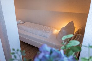A single bed with a pillow and a headboard, a bedside table, and a wall-mounted heater.