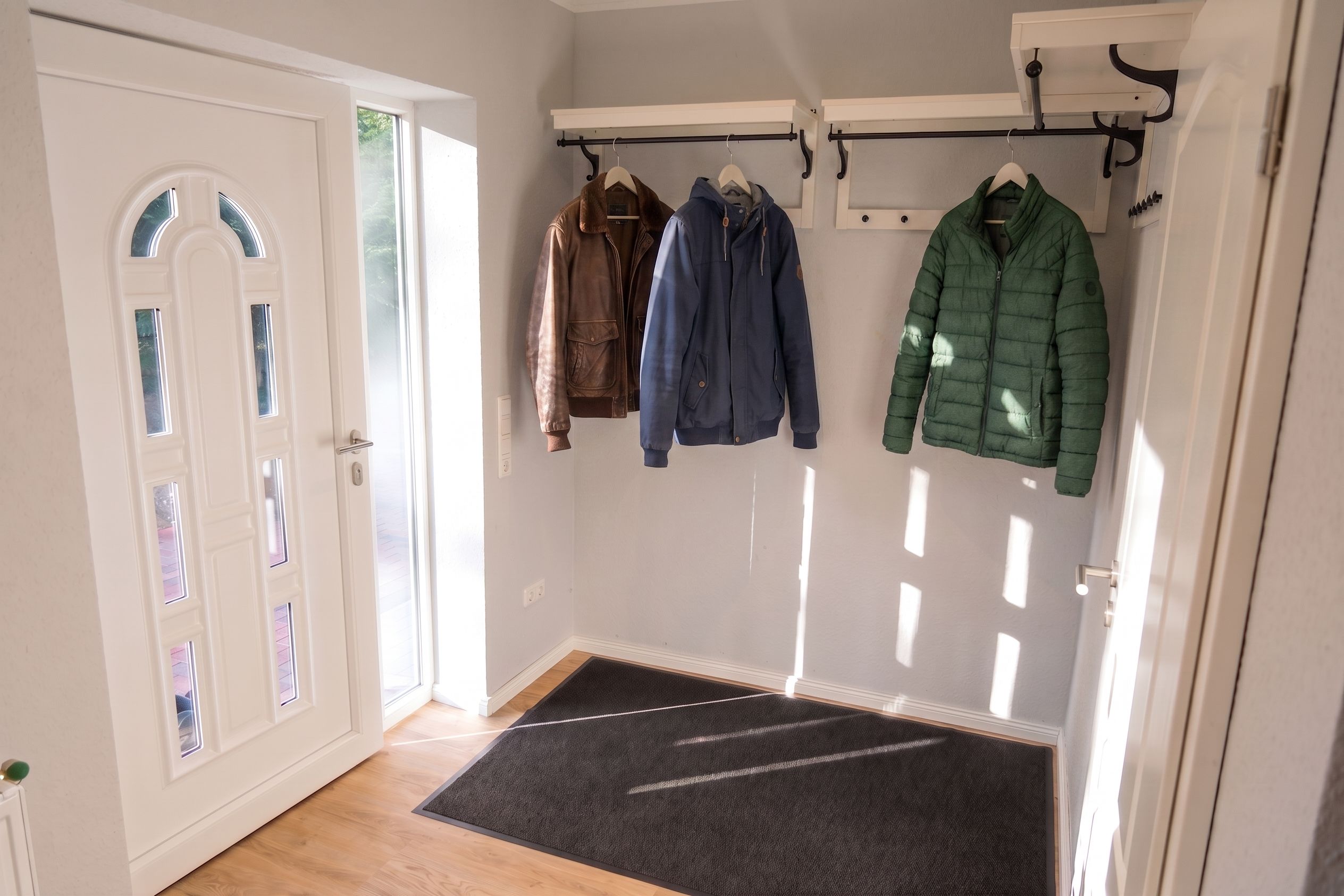 A hallway with a white door, a coat rack with several jackets, and a black doormat.