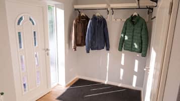 A hallway with a white door, a coat rack with several jackets, and a black doormat.