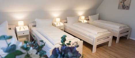 A room with three single beds, each with a bedside table and lamp, in a simple, clean design.