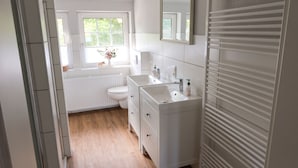 A modern bathroom with a white sink, toilet, and vanity. There is a window with a view of greenery outside.