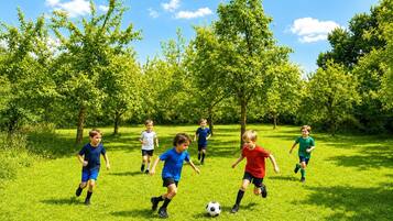 Children playing soccer on a grassy field with trees in the background.