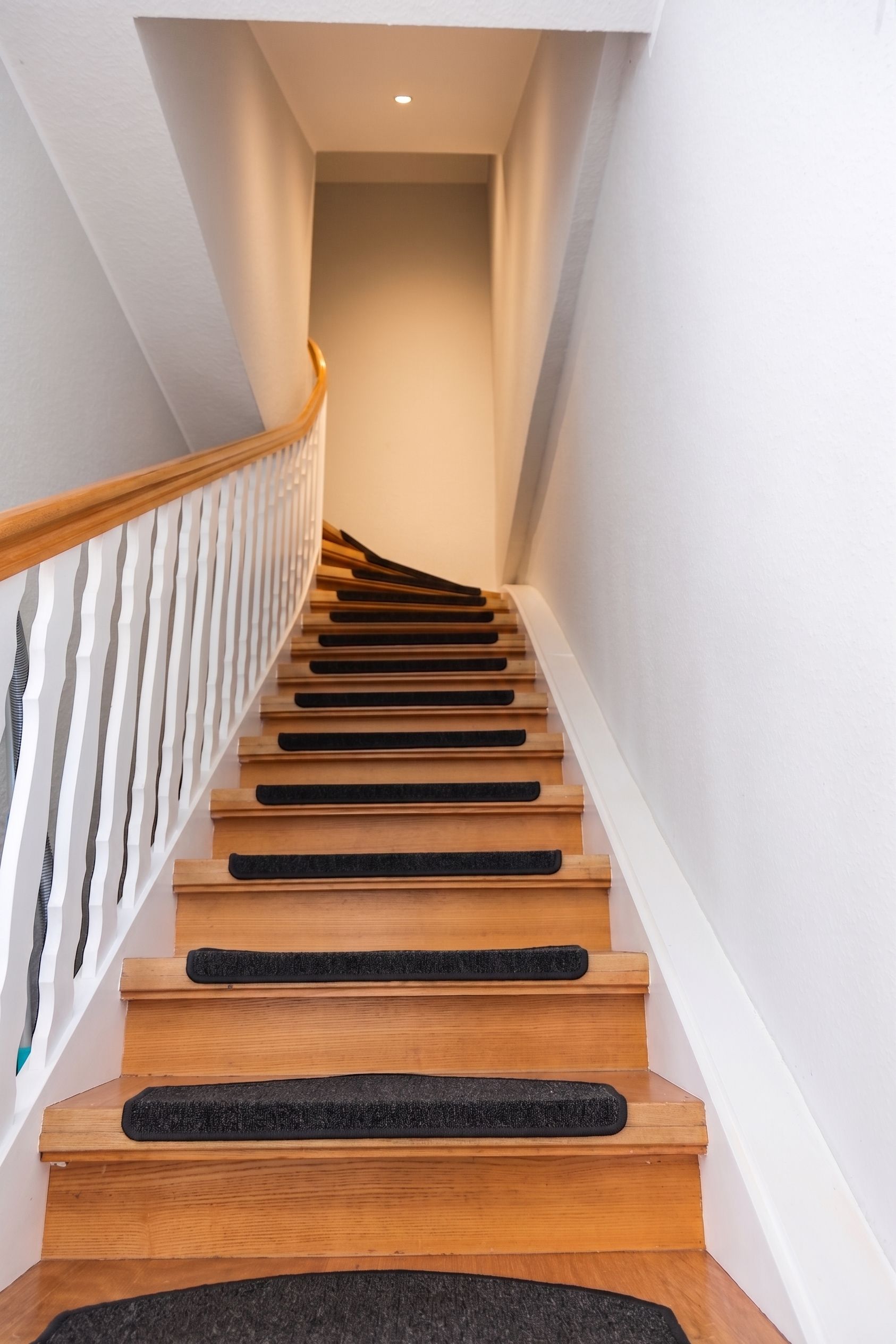 A wooden staircase with a white railing and black non-slip treads.